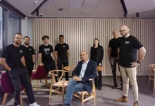 Diverse team of eight professionals posing together in a modern corporate office setting.