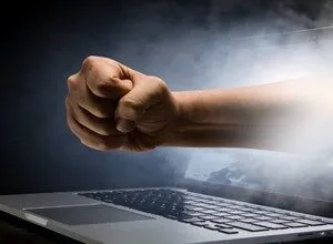 A clenched fist punches out from a laptop screen surrounded by smoke and dramatic lighting.