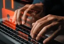 Close-up of hands typing on a laptop with glowing red security icons and a padlock graphic overlay.