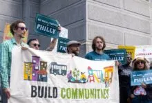 Activists holding a banner that reads BUILD COMMUNITIES NOT DATA CENTERS in front of a stone building.