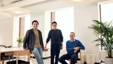 Three male founders standing and sitting together in a modern, brightly lit office space.