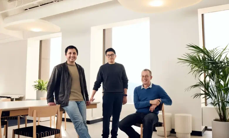Three male founders standing and sitting together in a modern, brightly lit office space.