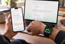 Person holding a smartphone and wearing a smartwatch with a laptop displaying text in the background.