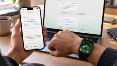 Person holding a smartphone and wearing a smartwatch with a laptop displaying text in the background.
