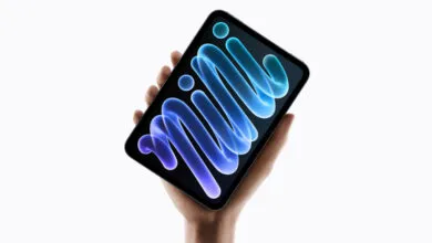 A hand holds an iPad mini featuring a vibrant blue abstract wallpaper against a solid white background.