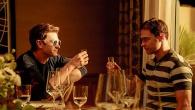 Two men seated at a restaurant table raise small shot glasses in a toast, bathed in warm indoor lighting.