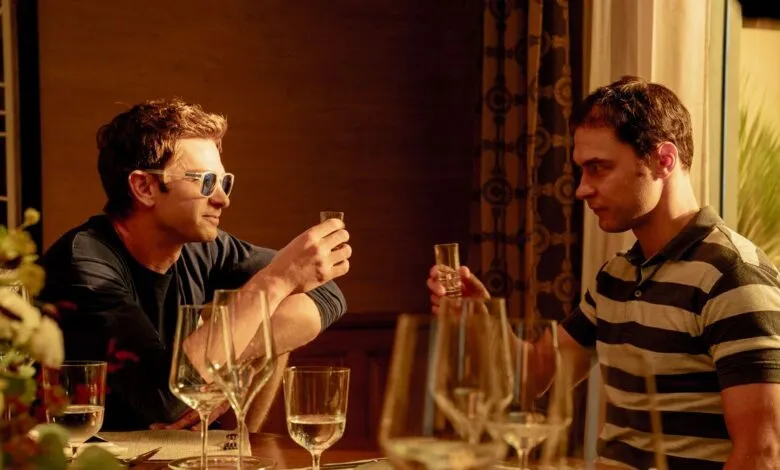 Two men seated at a restaurant table raise small shot glasses in a toast, bathed in warm indoor lighting.