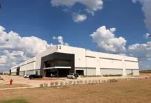 Modern white and black industrial warehouse building under a bright blue sky with fluffy white clouds.