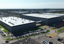 High-angle view of large industrial warehouse facilities with parking lots filled with cars.