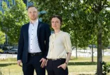 Benjamin Dose and Angela Relogio posing outdoors near a modern office building and leafy green trees.