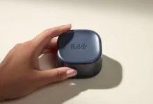 Hand holding a dark blue, square Brick app blocker device against a light background