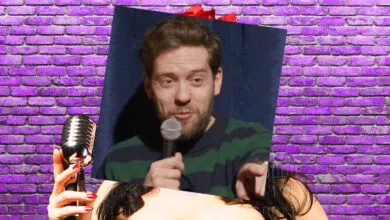 Comedian Jeremiah Watkins holds a microphone in front of a purple brick wall backdrop.