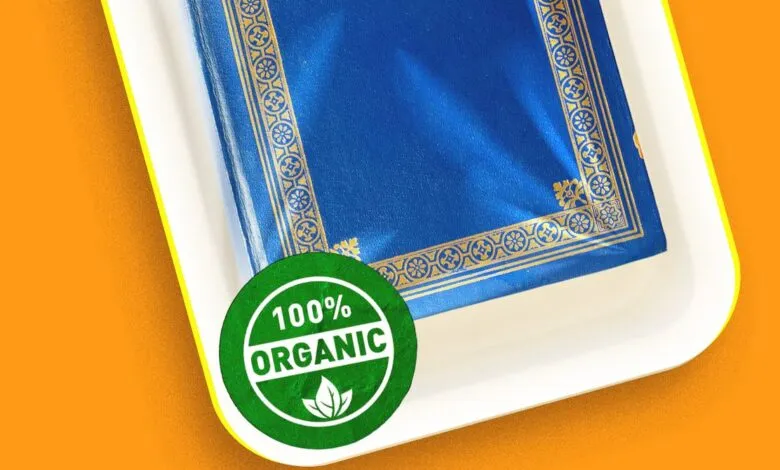 A blue book with gold trim packaged in a white tray with a 100% organic sticker on an orange background.