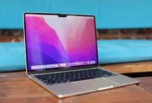 Silver MacBook Pro open on a wooden table with a vibrant pink and purple wallpaper displayed.