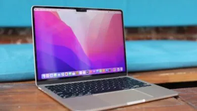 Silver MacBook Pro open on a wooden table with a vibrant pink and purple wallpaper displayed.