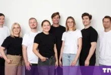 Group portrait of eight diverse professionals smiling together against a plain white wall.