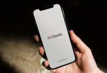 A hand holding a smartphone displaying the Claude AI app interface by Anthropic on a light background.