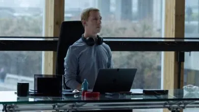 Actor Jefferson White sits at a sleek glass desk with a laptop and headphones in an office setting.