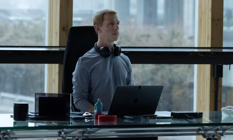 Actor Jefferson White sits at a sleek glass desk with a laptop and headphones in an office setting.