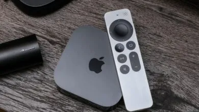 Apple TV box and silver remote resting on a dark wood grain table surface.
