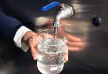 Water pouring from a stainless steel spigot into a Labinvo scientific beaker held by a person.