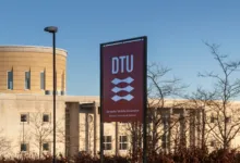Sign for the Technical University of Denmark (DTU) in front of modern campus buildings on a clear day.