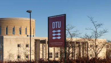 Sign for the Technical University of Denmark (DTU) in front of modern campus buildings on a clear day.
