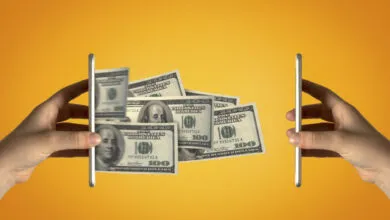 Two hands holding smartphones with US dollar bills transferring between them against a solid orange background.