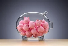 A large transparent glass piggy bank filled with numerous small pink ceramic piggy banks.