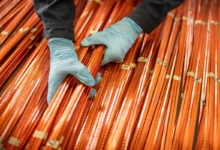 Worker in blue gloves handling long orange rods in a factory