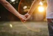 An elderly couple holding hands lovingly outdoors during a golden sunset.