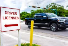 A roadside sign pointing left towards a driver license office with a black pickup truck passing by.