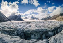 Vast, heavily crevassed Turner Glacier under towering granite peaks and a cloudy blue sky in Nunavut.