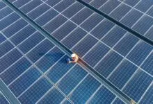 Top-down view of a technician working on a large solar panel array with a laptop.