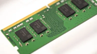 Close-up of a green computer RAM memory stick with black microchips and gold connector pins.