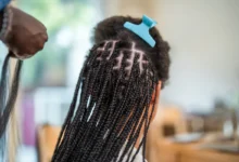 A hairstylist expertly braids extensions into a client's dark hair in a salon setting.
