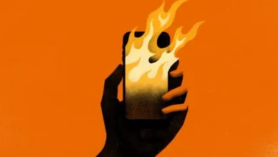 A dark silhouette of a hand holding a smartphone engulfed in yellow and orange stylized flames.