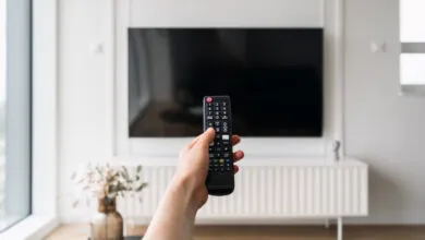 A person holds a remote control pointing toward a large wall-mounted smart television.
