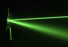 Vibrant green laser beams passing through optics in a dark room, scattering light particles.