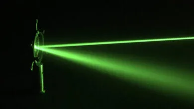 Vibrant green laser beams passing through optics in a dark room, scattering light particles.