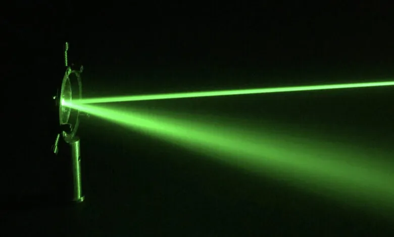 Vibrant green laser beams passing through optics in a dark room, scattering light particles.