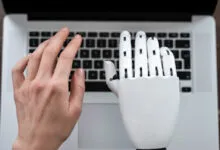 Human hand and white robotic hand positioned over a laptop keyboard