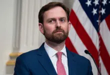 FTC Chairman Andrew Ferguson wearing a blue suit and red tie with an American flag background
