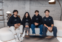 Four diverse young adults posing together on a white couch wearing branded Ghost hoodies.