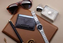 Flat lay of men's accessories including sunglasses, wallet, watch, pen, and perfume.