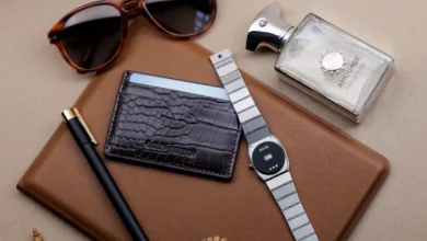 Flat lay of men's accessories including sunglasses, wallet, watch, pen, and perfume.
