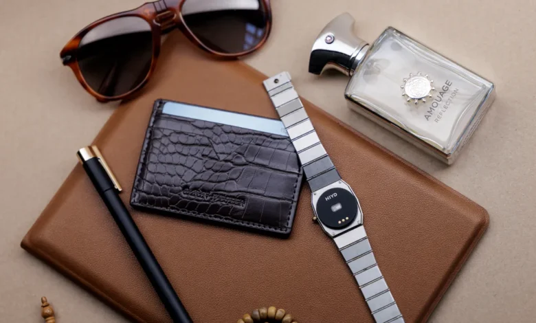 Flat lay of men's accessories including sunglasses, wallet, watch, pen, and perfume.