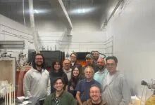 A diverse group of researchers and engineers pose together in a bright industrial laboratory.