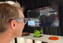 A person wearing smart glasses looks at a monitor displaying data and interactive prompts.