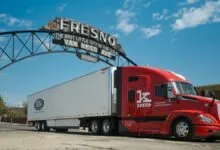 A red Kodiak AI autonomous semi-truck drives beneath the historic Fresno arch sign.